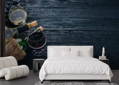 A bottle of wine with glasses and grapes on a black wooden background. Free space for text. Top view. Wall mural