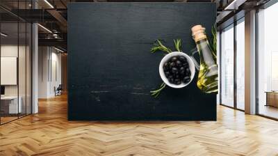 A set of olives and olive oil and rosemary. Green olives and black olives. On a black wooden background. Free space for text. Wall mural