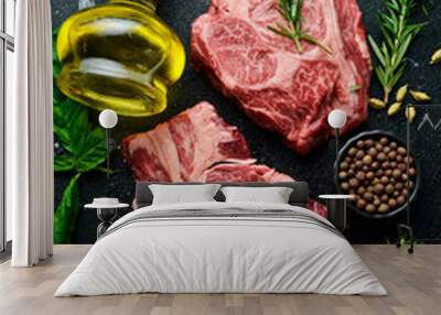 Two Raw rib eye steaks on a wooden board with spices. Free space for text. On a black stone background. Wall mural