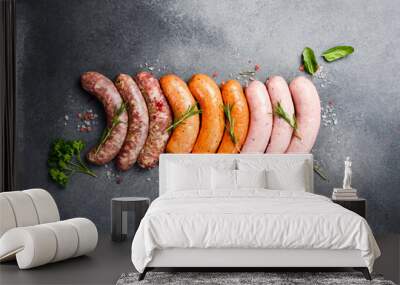 Uncooked mix of barbecue sausages: beef, pork and chicken sausages. On a gray concrete background. Top view. Wall mural