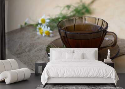 dark glass cup of Herbal tea with chamomile tea on sackcloth on a light wooden table with copy space. cup fo tea with bouquet fresh flowers and green leaves on yellow background Wall mural