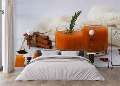 two glasses of fresh pumpkin or oranges juice with slices of pumpkin, spices on a white background. fresh cocktail with sprig of rosemary and sticks of cinnamon with warm white plaid on white table.  Wall mural