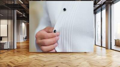 A man fastens his shirt. White shirt with buttons on the body. Black buttons on a white men's shirt. Close-up hands button up shirt. Morning groom. Wall mural