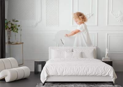 Portrait Little pretty smiling girl in white dress playing in white room Wall mural