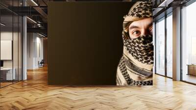 Portrait of arab man in keffiyeh on face. with a sad face in a military jacket and a headdress from the national keffiyeh on a black background Wall mural