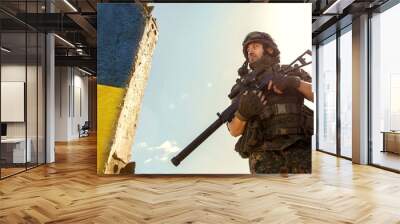 Ukrainian Soldier military in the war with a weapon in his hands. The flag of Ukraine is painted on a brick wall. Relations between Ukraine and Russia Wall mural