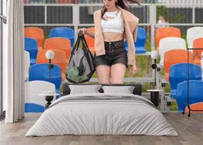 Confident woman in casual workout attire descending stadium steps with a bag, symbolizing readiness and determination. Concept: Highlighting the significance of incorporating exercise into daily Wall mural