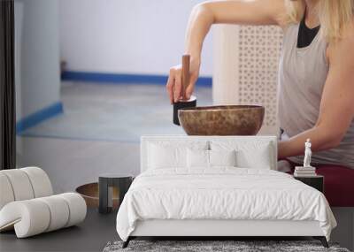 Woman playing on Tibetan singing bowl while sitting on yoga mat. Vintage tonned. Wall mural