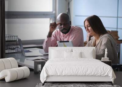 young African-American man with female colleague while working in cubicle at office. Ethnic entrepreneurs planning their work using laptop and cell phone. Staff relationship concept. selective focus Wall mural