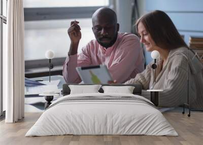 young African-American man with female colleague while working in cubicle at office. Ethnic entrepreneurs planning their work using laptop and cell phone. Staff relationship concept. selective focus Wall mural