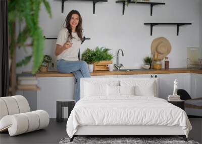 Young beautiful modern woman sitting on counter in the kitchen at home. Wall mural