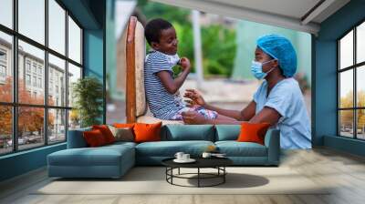 cheerful african nurse in protective face mask seeing a child outdoor-concept on child health care i Wall mural