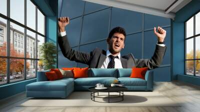 Young successful businessman celebrating a goal on a modern building background Wall mural