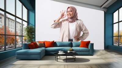 Portrait of excited Asian hijab woman in casual suit showing ok hand gesture and smiling looking at camera. Advertising concept. Isolated image on white background Wall mural