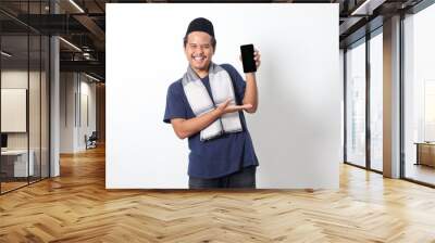 Portrait of excited Asian muslim man wearing sarung scarf showing blank screen mobile phone mockup while pointing and presenting product. Social media concept. Isolated image on white background Wall mural