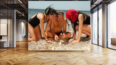 a man with two women are searching in the sand by the sea Wall mural