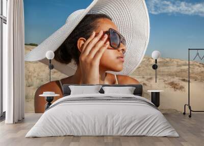 dark-skinned woman in sunglasses walks along the sand in the desert in the summer Wall mural