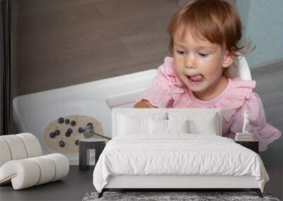 Happy, smiling child eating oatmeal with berries. The concept of a healthy breakfast for children, porridge with blueberries on baby chair Wall mural