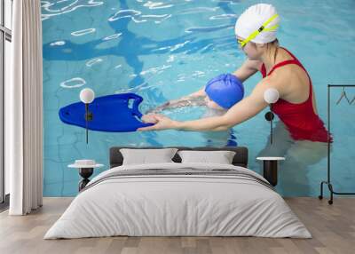 Little boy using the kickboard for learning to swim with trainer in the swimming pool Wall mural