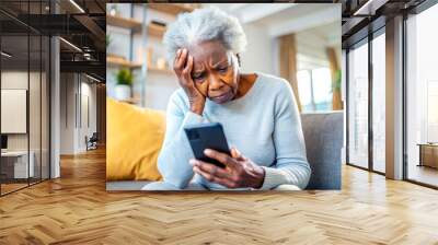 Nervous confused elderly senior afro woman stressed worried with smartphone. Frustrated black granny having problem with paying, buying online and payments. Internet fraud or scams  Wall mural