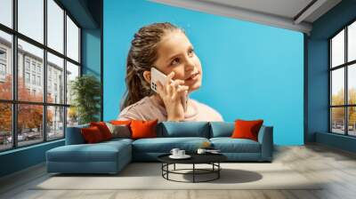 A beautiful teenage girl uses a smartphone against a blue wall. Summer concept. Buzzer generation style. The concept of social networks and mobile communication Wall mural