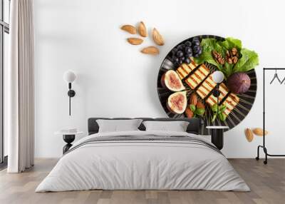 Fried slices of halloumi cheese on a dark, round plate with fruit, nuts and salad leaves on a white background. Traditional cheese of Greece and Turkey. copy space. flat lay. Wall mural