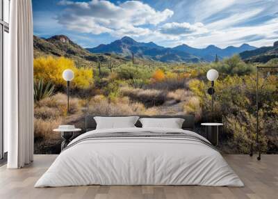 A scenic view of a vibrant desert landscape featuring mountains, colorful vegetation, and a blue sky with fluffy clouds. Wall mural