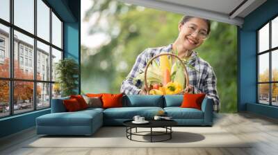 Beautiful young brunette Portrait Famer Woman hand holding Vegetables in the bamboo basket on green Farming Plant at sunset background ,Organic fresh harvested vegetables; Wall mural