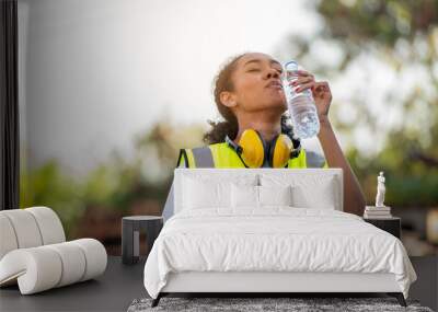 Divergent A African american woman foreman or worker wearing Cross Eye safety is drinking a bottle of water after finishing work and relaxing on the old truck at cargo container port Wall mural