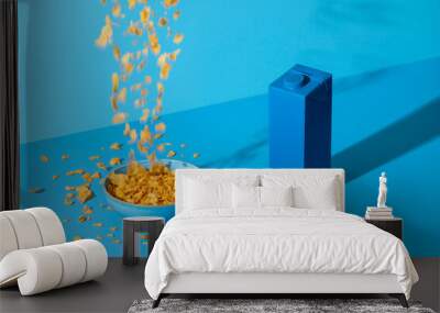 Pouring cornflakes cereals in a bowl on a blue table. Breakfast table in natural light. Wall mural