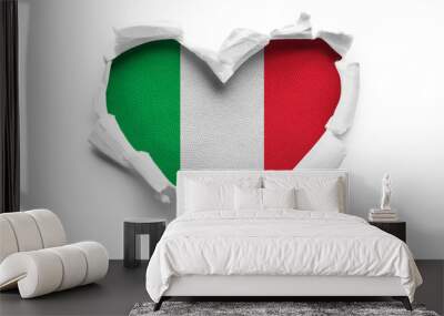 Heart shaped hole torn through paper, showing satin texture of flag of Italy. Isolated on white background Wall mural