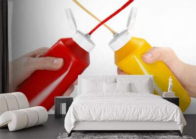 Two hands squeezing ketchup and mustard out of plastic bottles, isolated on white Wall mural