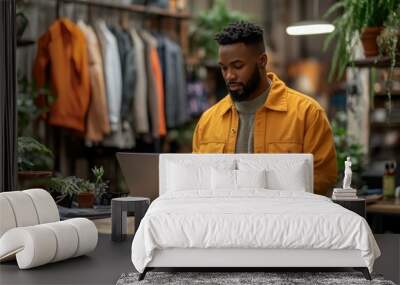 Black man in casual attire working on a laptop, with accessories on a table Wall mural