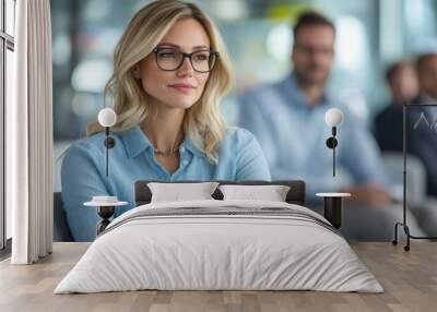 Blonde businesswoman in glasses holding a tablet, thinking during office meeting discussion Wall mural