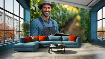 Handsome man using a digital tablet in a vineyard, writing, smiling, professional work setting Wall mural