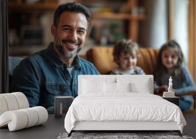 Happy father with a tablet, sitting on a chair in a modern living room, children playing nearby Wall mural