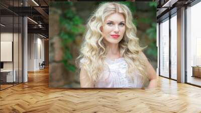 Portrait of a beautiful young blonde woman with long hair in a white dress on a background of a stone wall in nature. Soft focus Wall mural