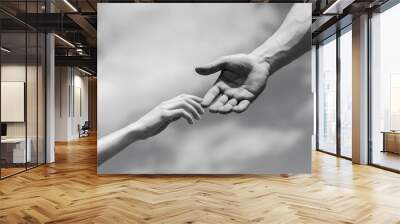 Giving a helping hand. Hands of man and woman on blue sky background. Lending a helping hand. Solidarity, compassion, and charity, rescue. Black and white Wall mural