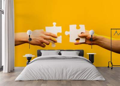 Two hands trying to connect couple puzzle piece on yellow background. Teamwork concept. Holding puzzle. Closeup hand of connecting jigsaw puzzle. Business solutions, success and strategy concept Wall mural