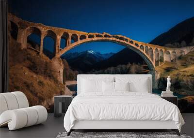 Historic stone bridge spans serene river, illuminated under night sky with mountains in background Wall mural