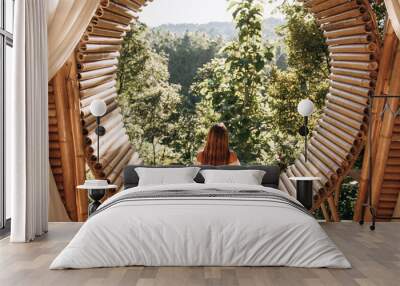 Attractive girl enjoys a beautiful view while sitting on a bamboo terrace overlooking the jungle in the mountains. Bamboo house in the mountains. Ecological housing Wall mural