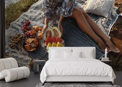 Beautiful women seat near picnic on the beach at sunset in boho style. Organic fresh fruit on linen blanket. Vegetarian eco idea for weekend picnic Wall mural