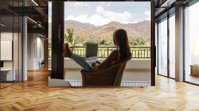 Freelancer, remote work, work from home. Young woman is working on a laptop on her balcony overlooking the tropical garden Wall mural