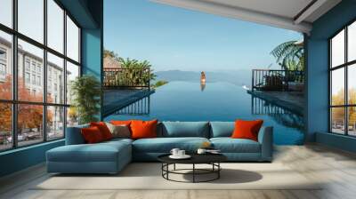 Slim young woman in swimsuit relaxing on edge tropical infinity pool in mountains. Palms around and crystal clean water. Luxury resort on Bali island Wall mural