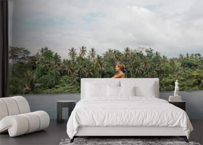 Slim young woman in swimsuit relaxing on edge tropical infinity pool with tropical coconut palm trees on background. Luxury resort on Bali island Wall mural