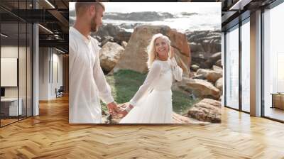 Stylish Romantic wedding couple against the background of the ocean and stones. Follow me. Bride holds the bridegroom's hand Wall mural