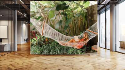 Woman lying in a hammock in a garden and enjoying a book reading in tropical hotel resort Wall mural