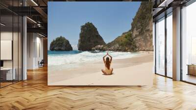 Young girl in a yellow swimsuit practices yoga on a tropical beach with white sand and turquoise water. Vacation trip to Diamond Beach in Nusa Penida Bali Indonesia Wall mural