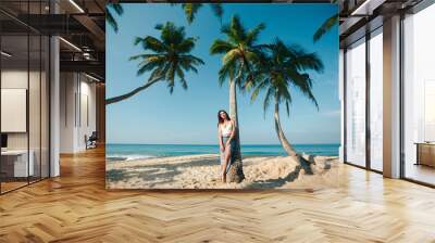 Young woman i sitting on palm trees. Young brunette lady relaxing on the tropical beach Wall mural