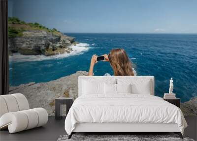 young woman on the beach taking picture on her phone Wall mural